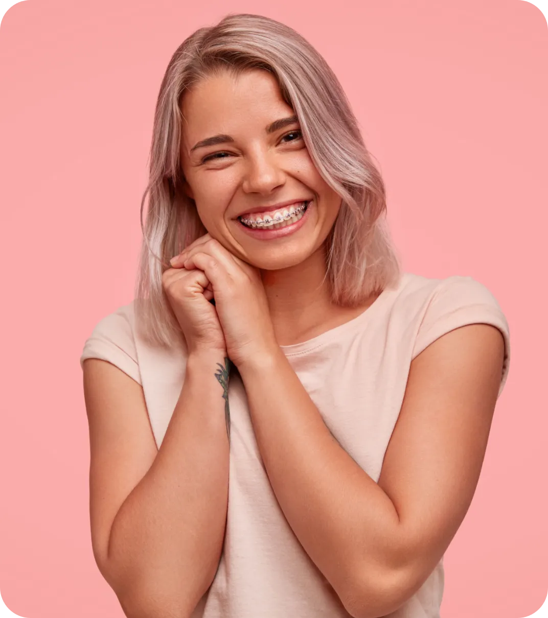 Femeie tânără cu păr blond deschis și aparat dentar, zâmbind fericit pe fundal roz