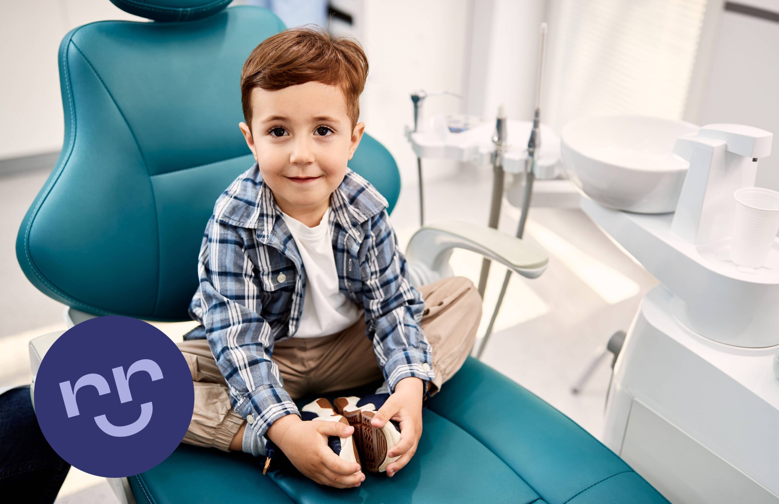 Băiețel zâmbitor, așezat pe scaunul stomatologic, la prima vizită la dentist